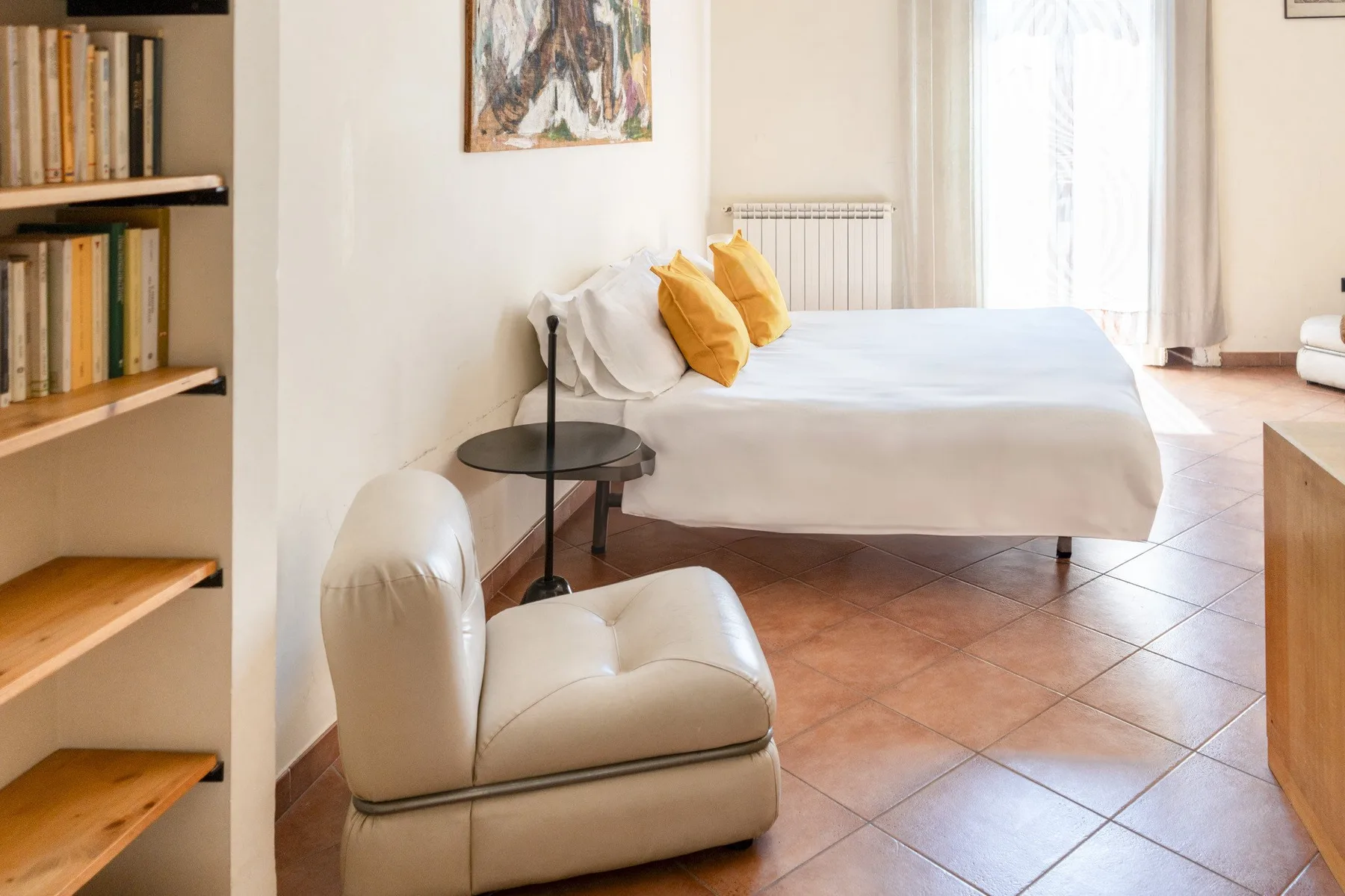 A bright bedroom with a neatly made bed and a cushioned chair.