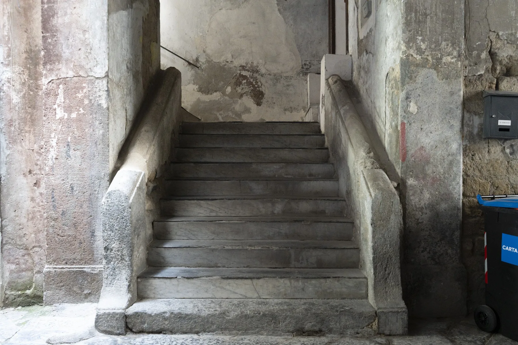 A stone staircase rises between worn plaster walls in a dim interior.
