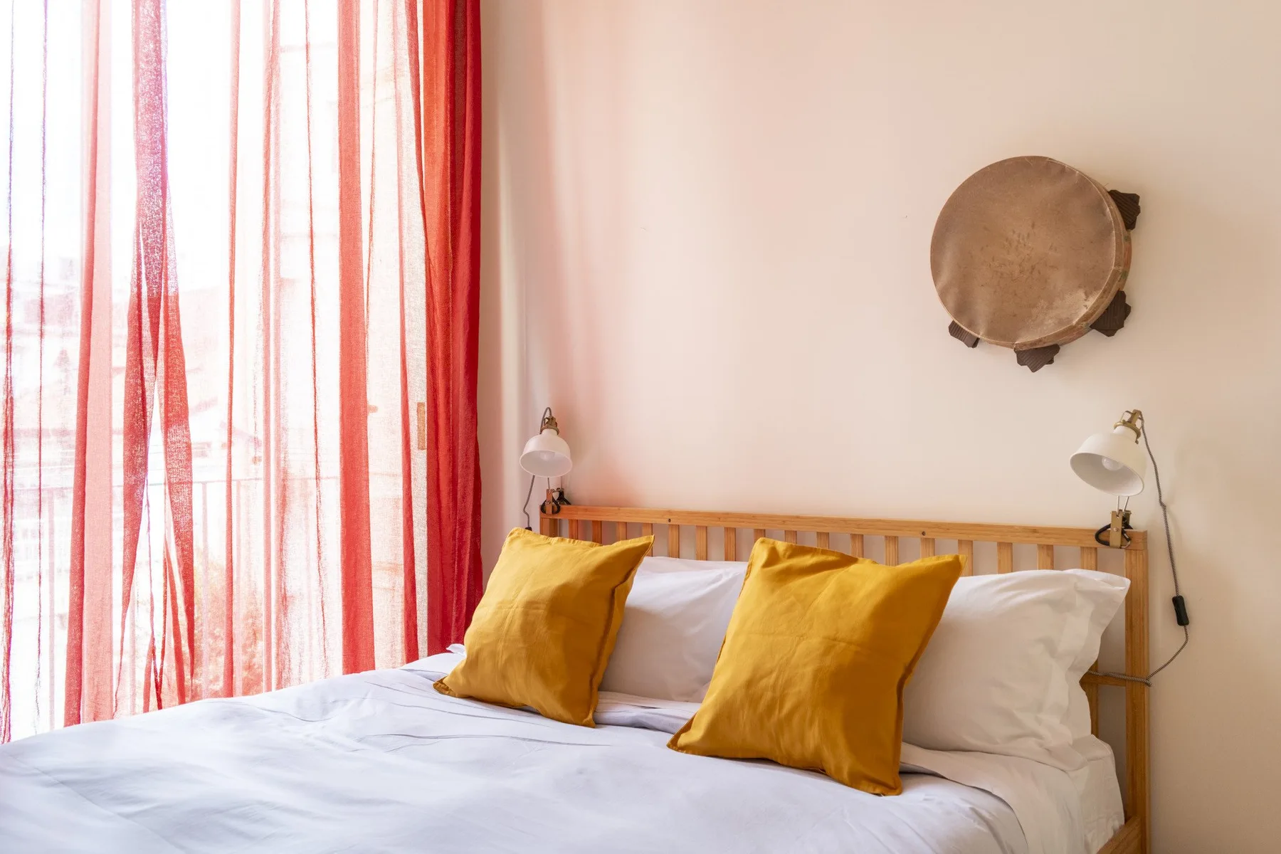 A bedroom with a wooden bed, white bedding, and yellow pillows beside a curtained window.