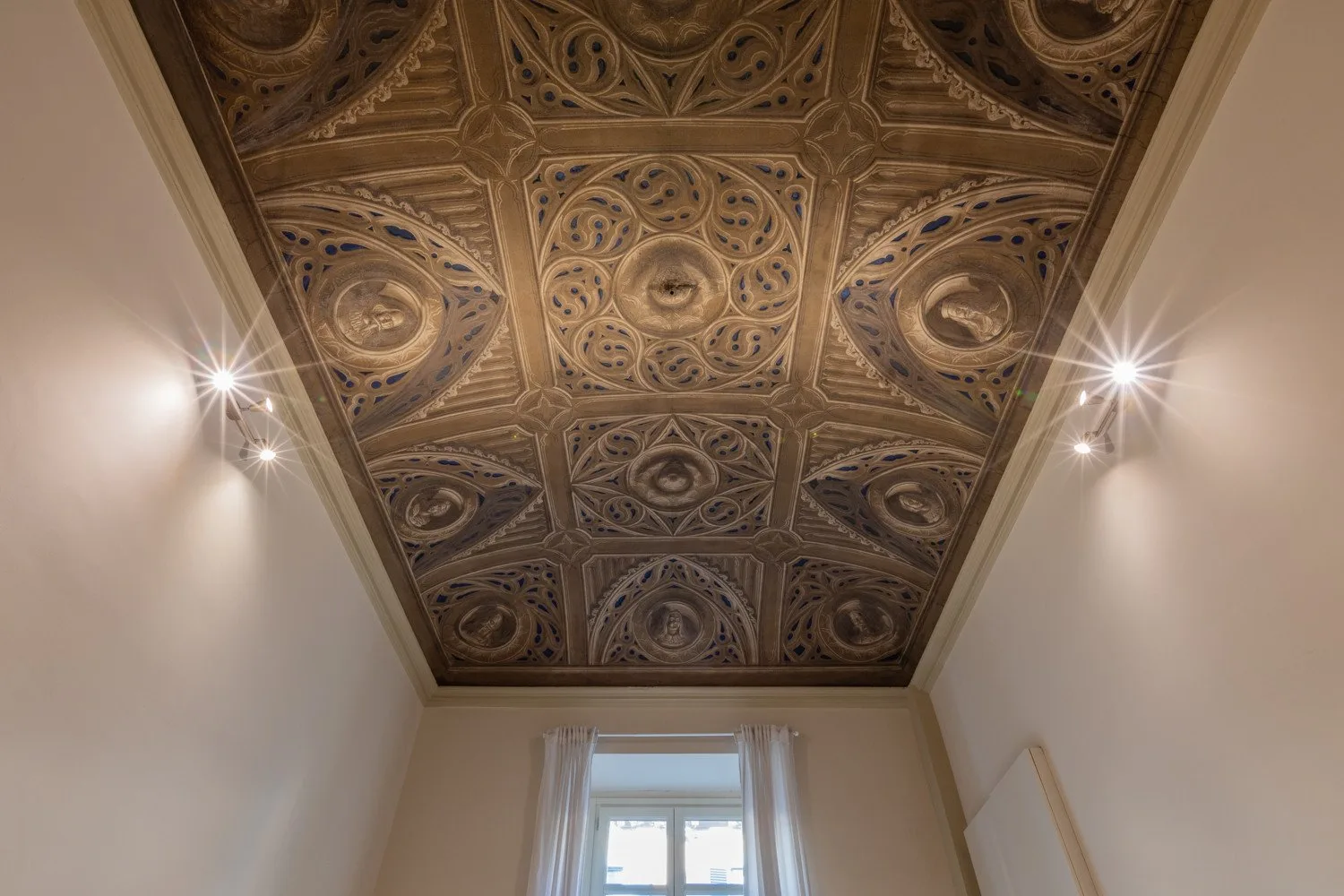 Una habitación con un techo ornamentado y una ventana.