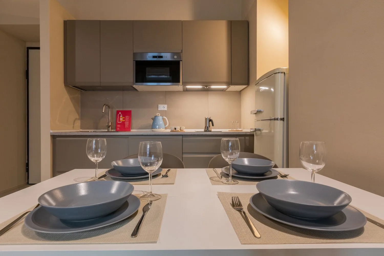Una mesa puesta con platos y copas frente a una cocina compacta.