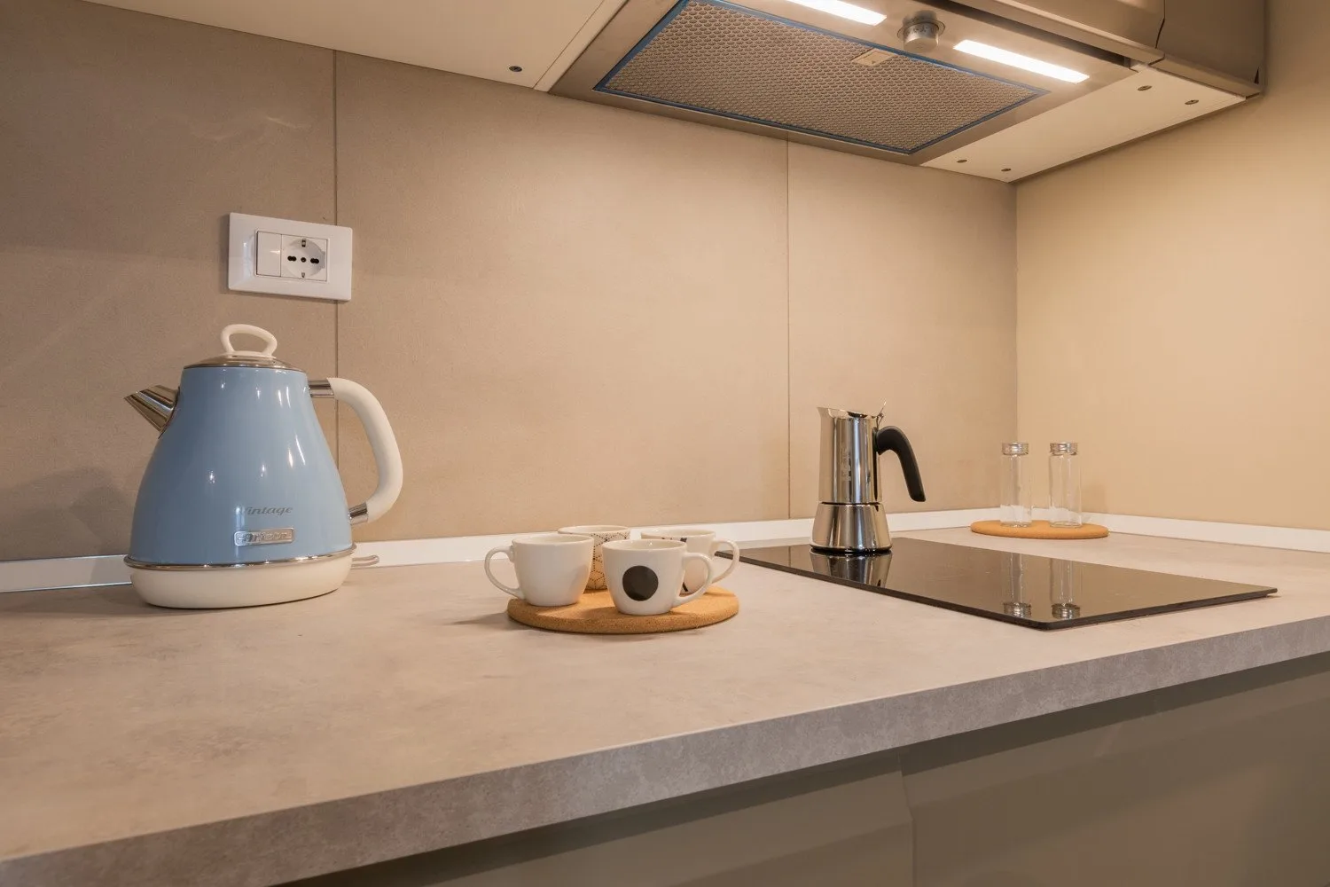 Una encimera de cocina tiene una tetera azul, tazas y una placa de cocción.