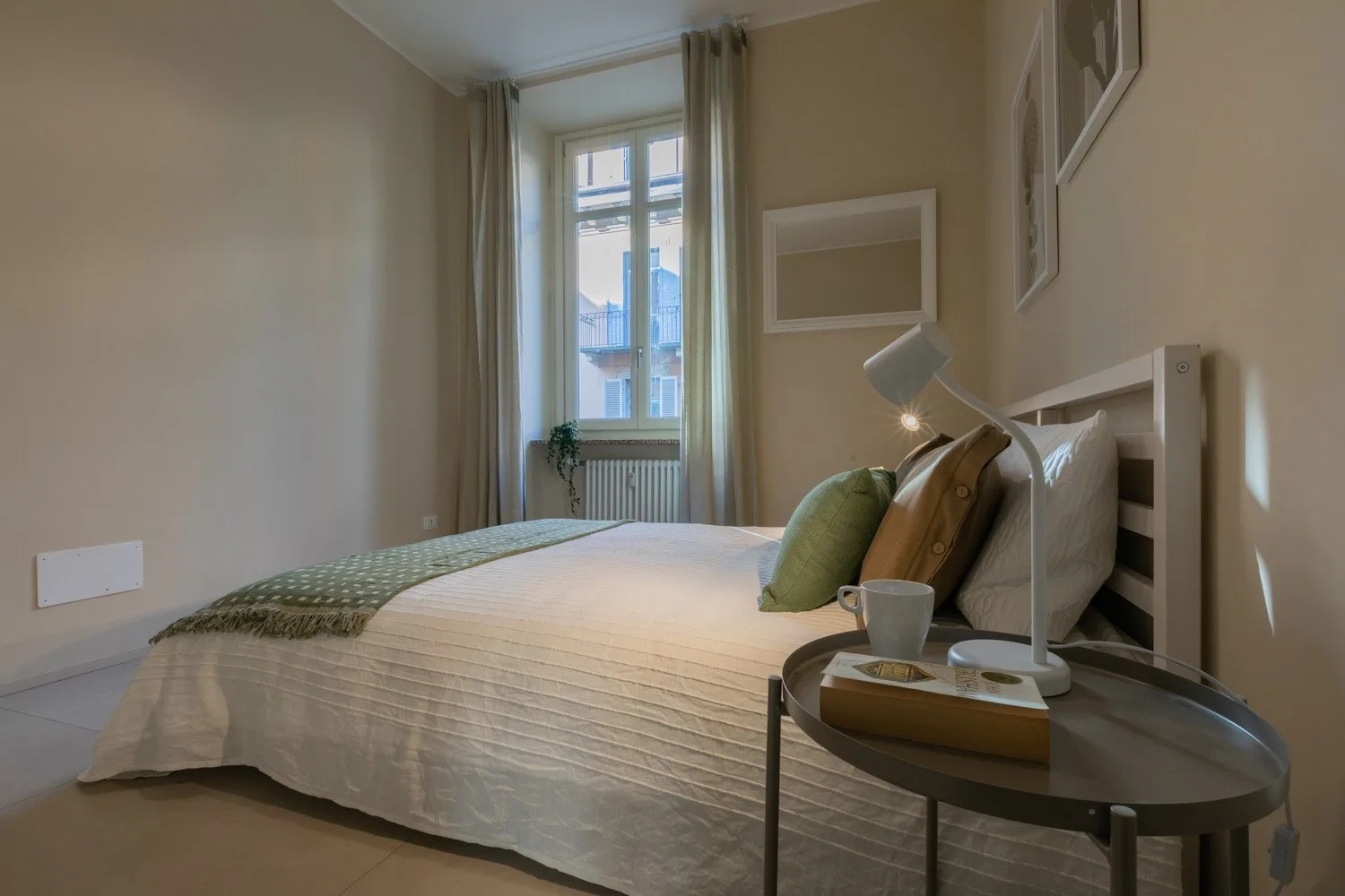 Un dormitorio con una cama bien arreglada junto a una ventana y una mesita.