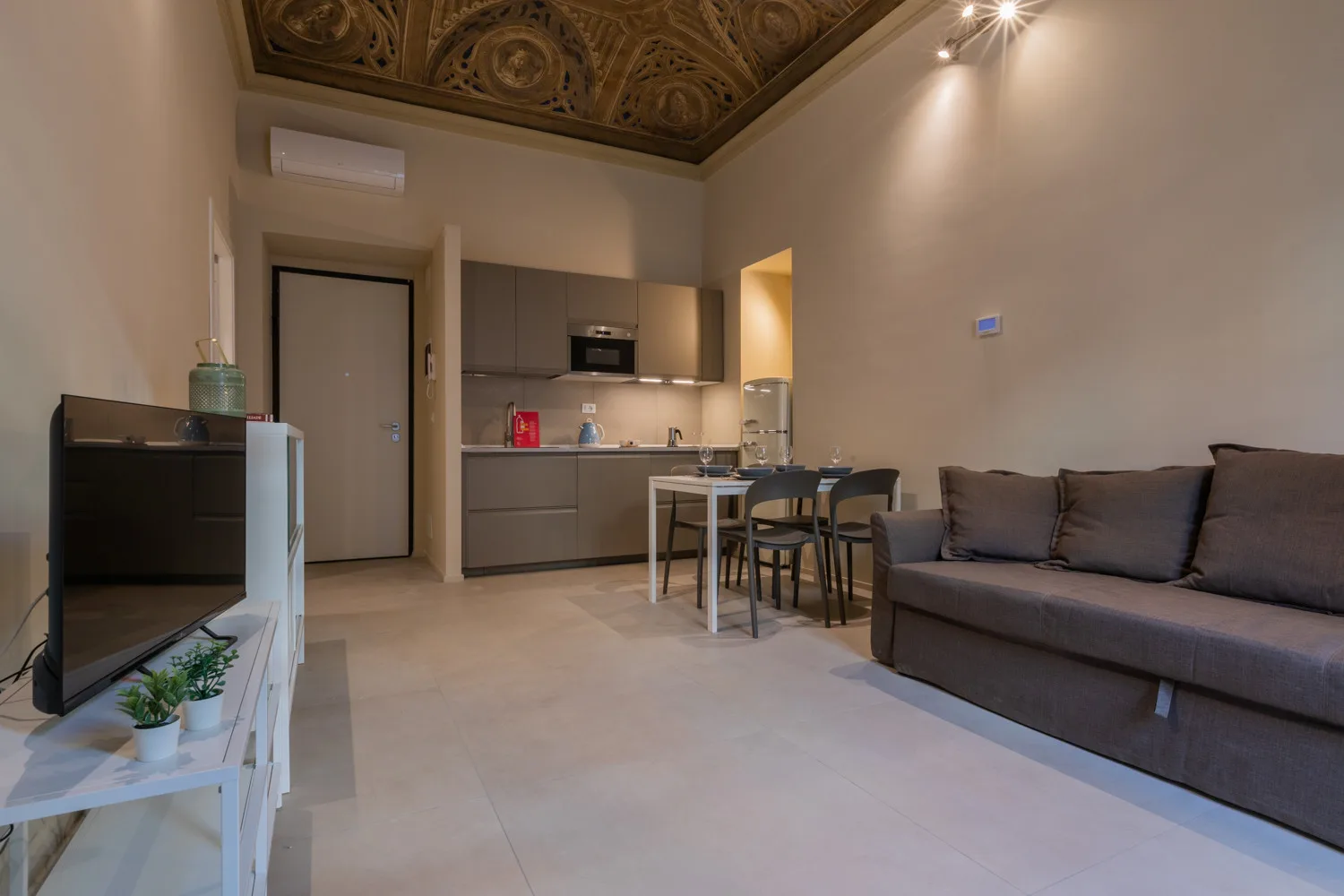Sala de estar con una pequeña cocina, mesa de comedor y sofá.