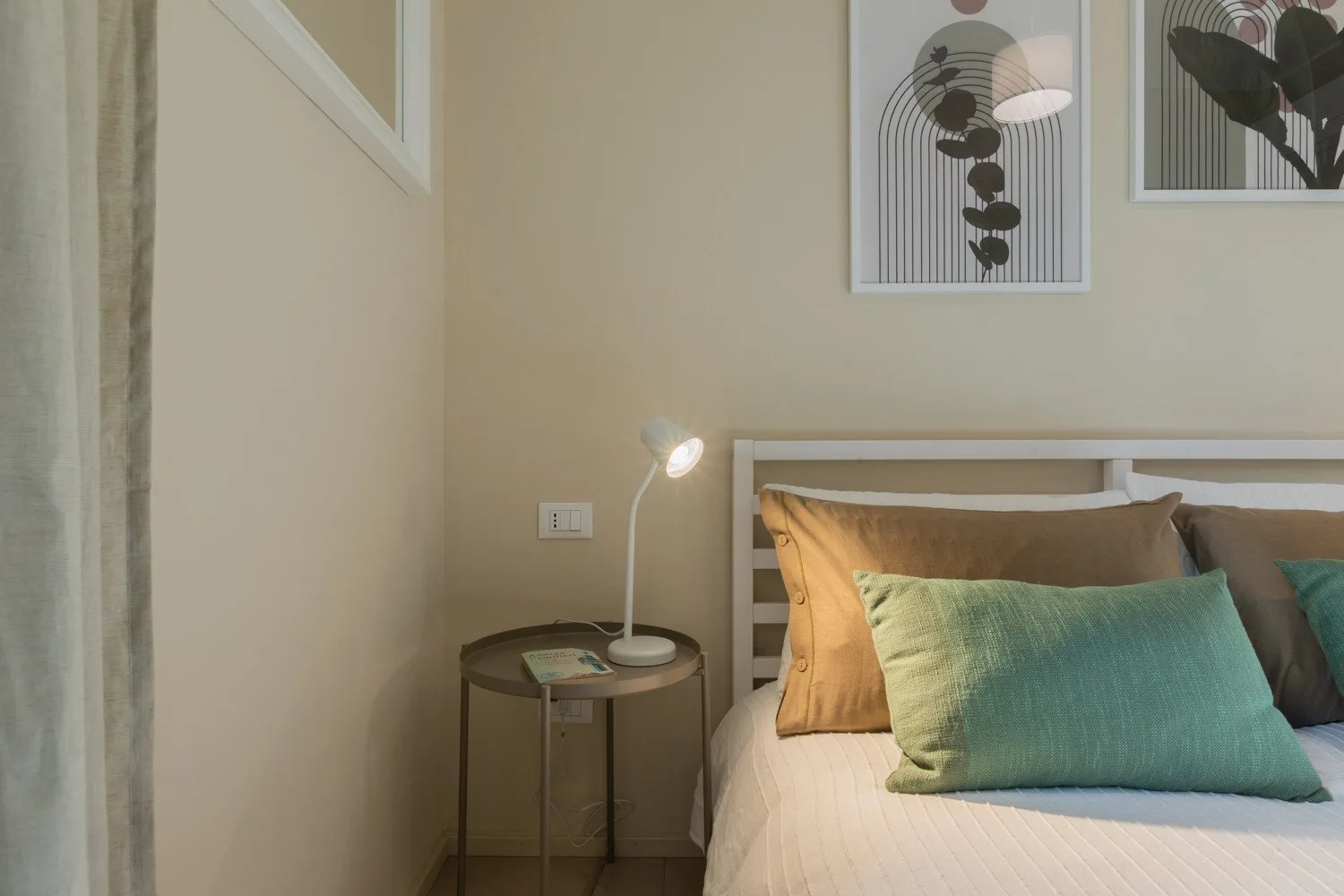 Un dormitorio con una cama, una mesa auxiliar y láminas botánicas enmarcadas.