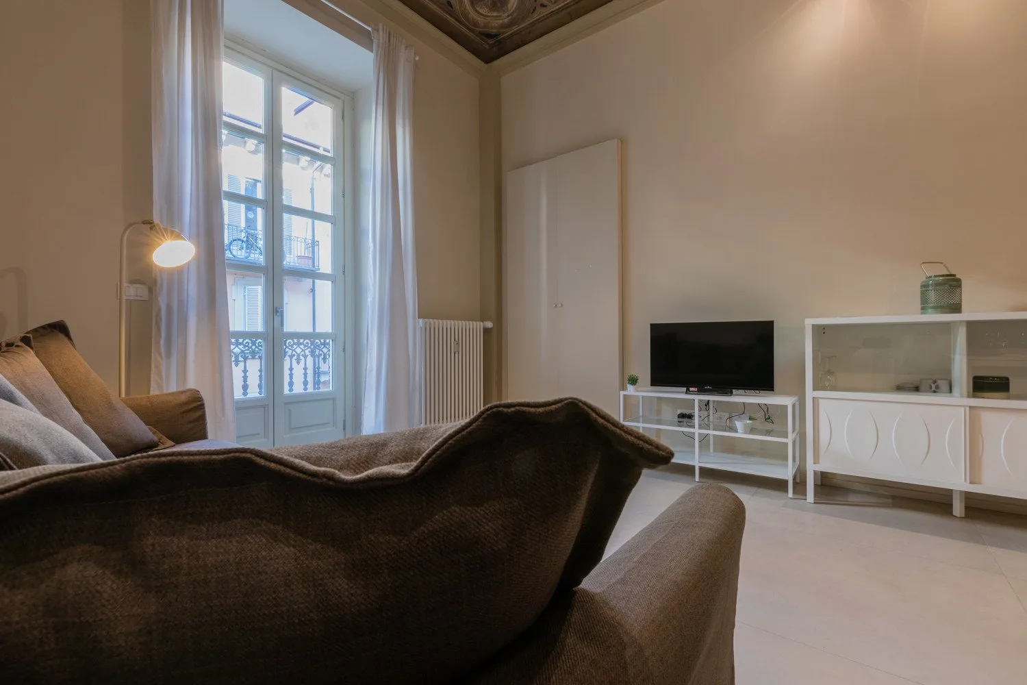 Una sala de estar con sofá, televisor y ventanas altas.