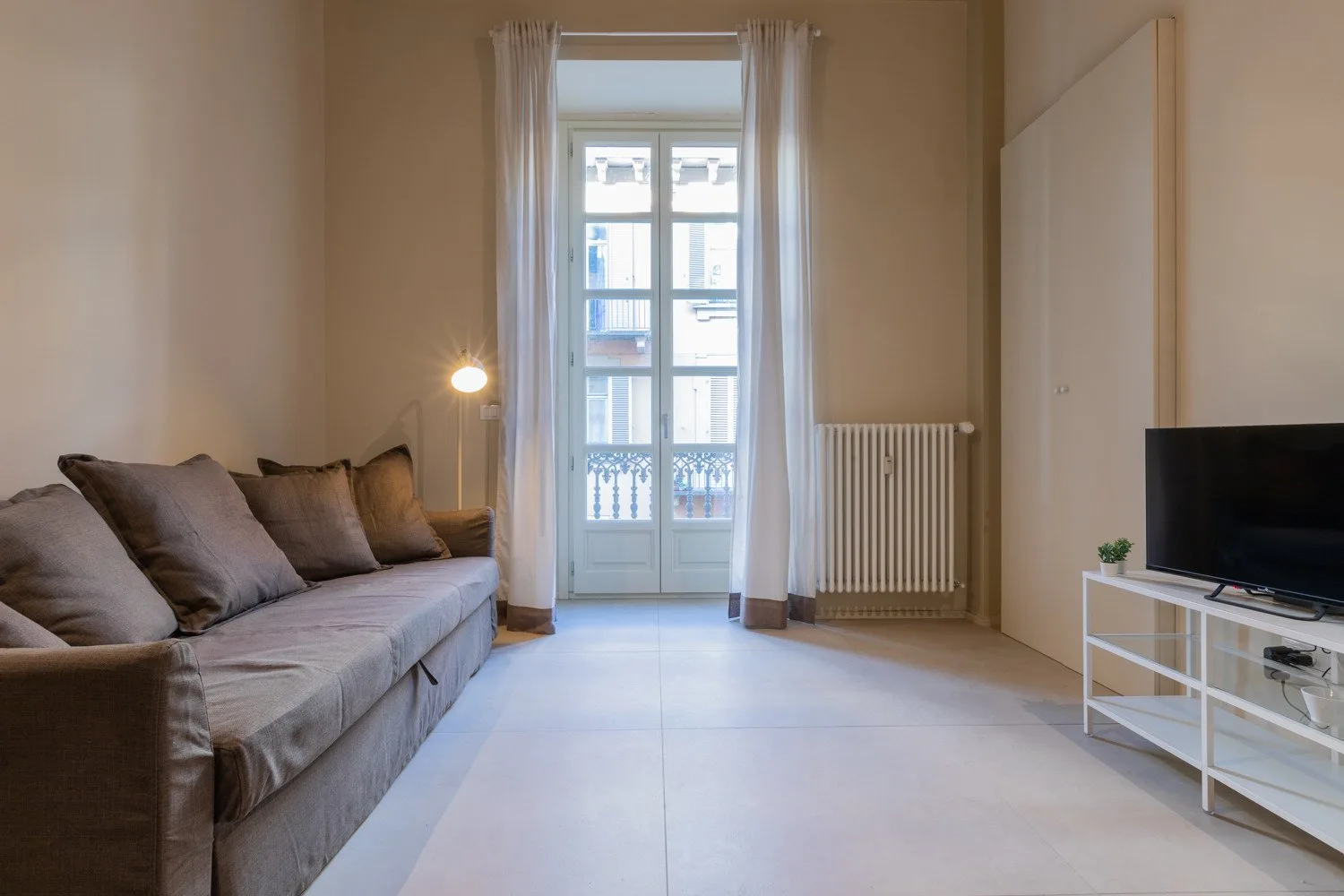 Una sala luminosa con asientos, un televisor y puertas altas de vidrio.