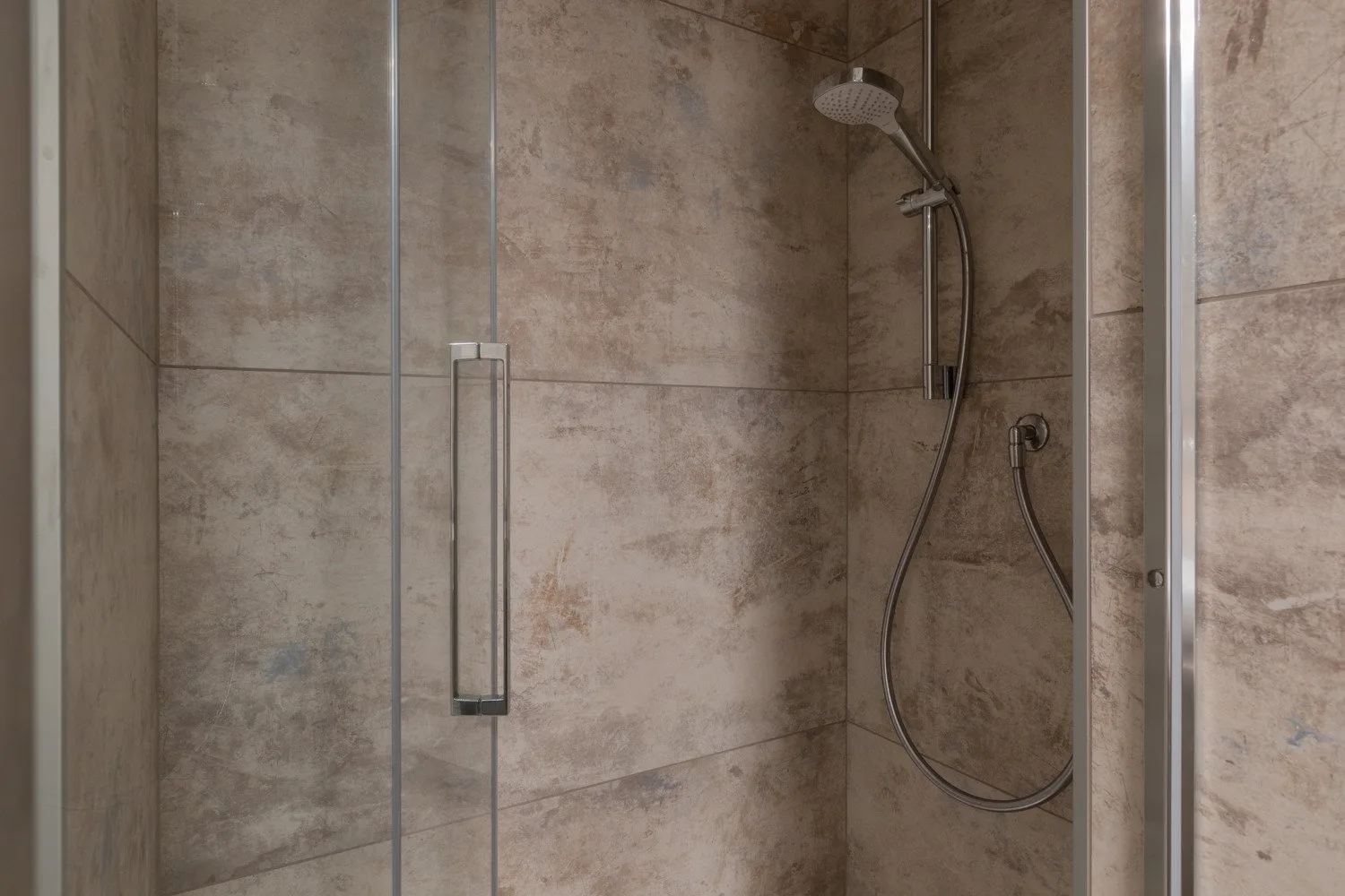Una ducha con azulejos, ducha de mano y paneles de vidrio.