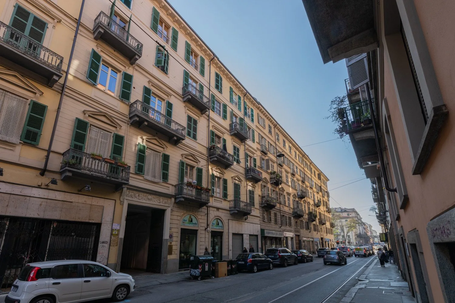 Una calle urbana flanqueada por edificios de apartamentos, balcones y coches aparcados.