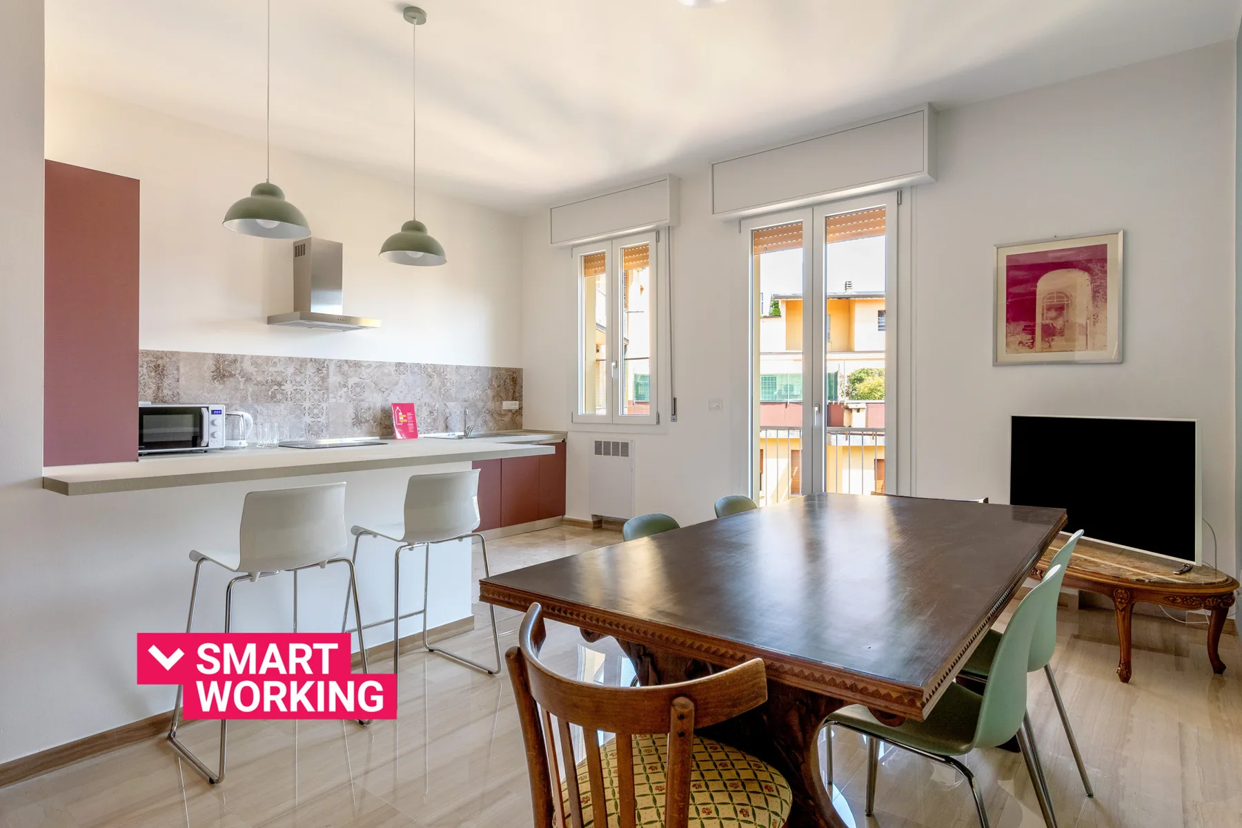 Zona de comedor y cocina con una mesa grande, una encimera y puertas al balcón.
