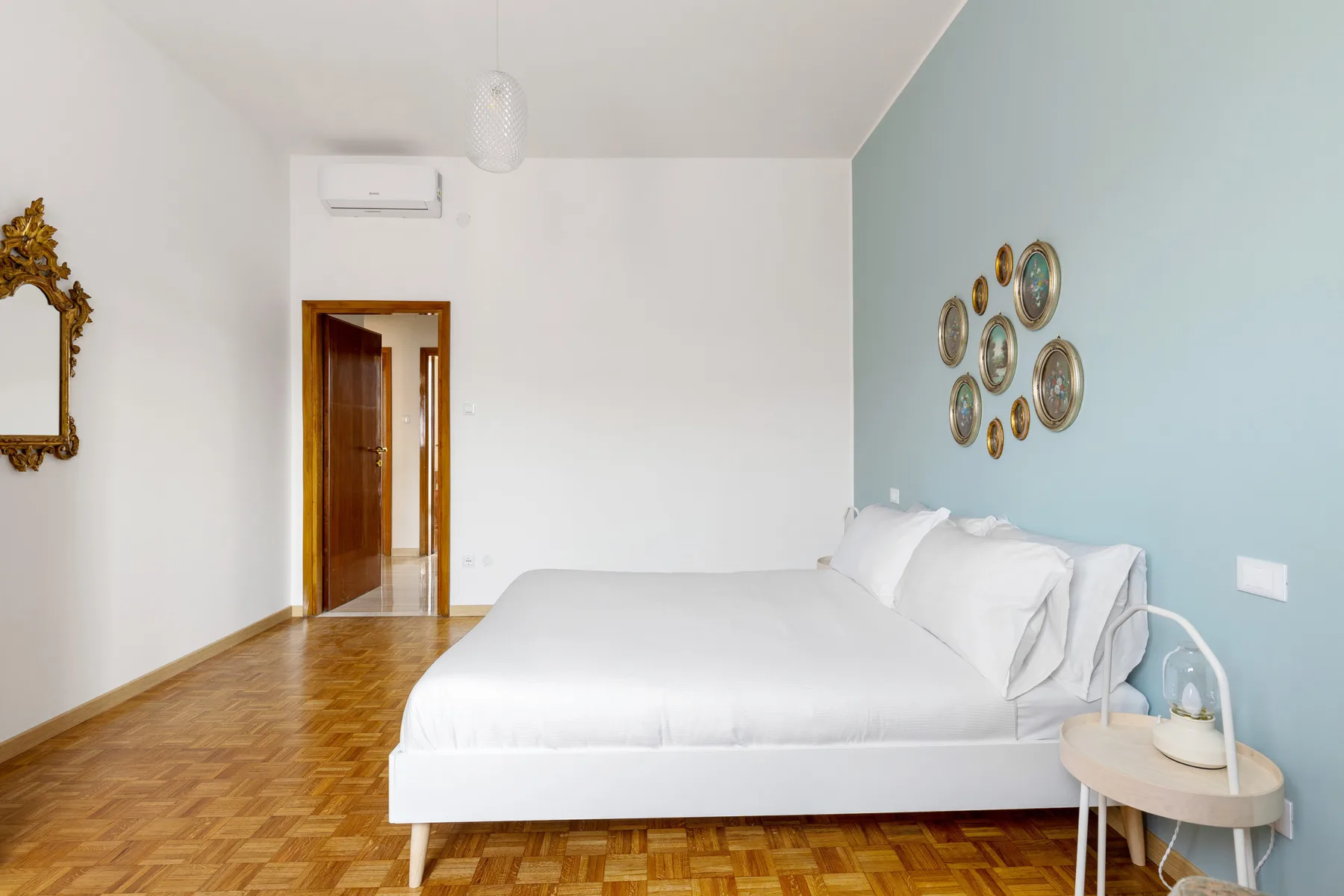 Un dormitorio con una cama blanca, una pared azul claro y suelo de madera.