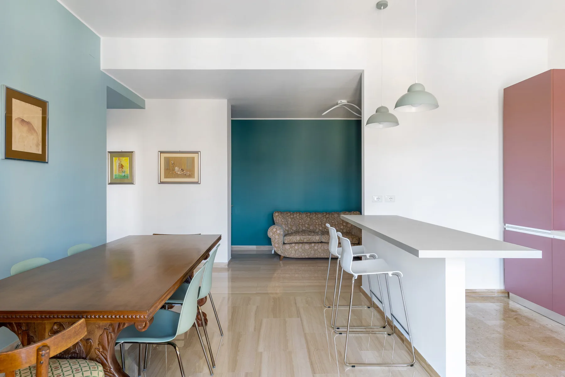 Un comedor con una larga mesa de madera y sillas junto a una barra blanca.