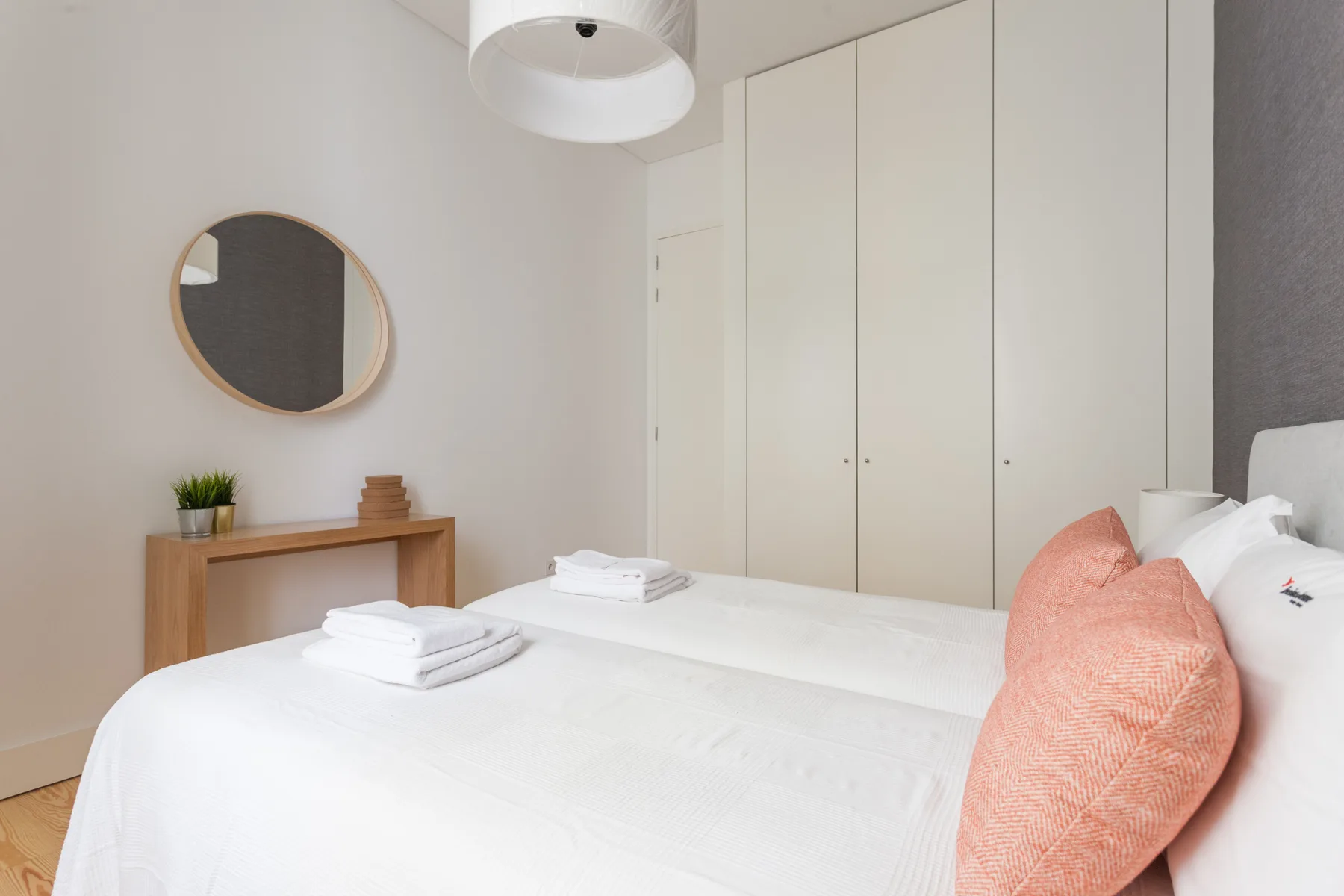 Un dormitorio con una cama bien hecha y un espejo redondo en la pared.