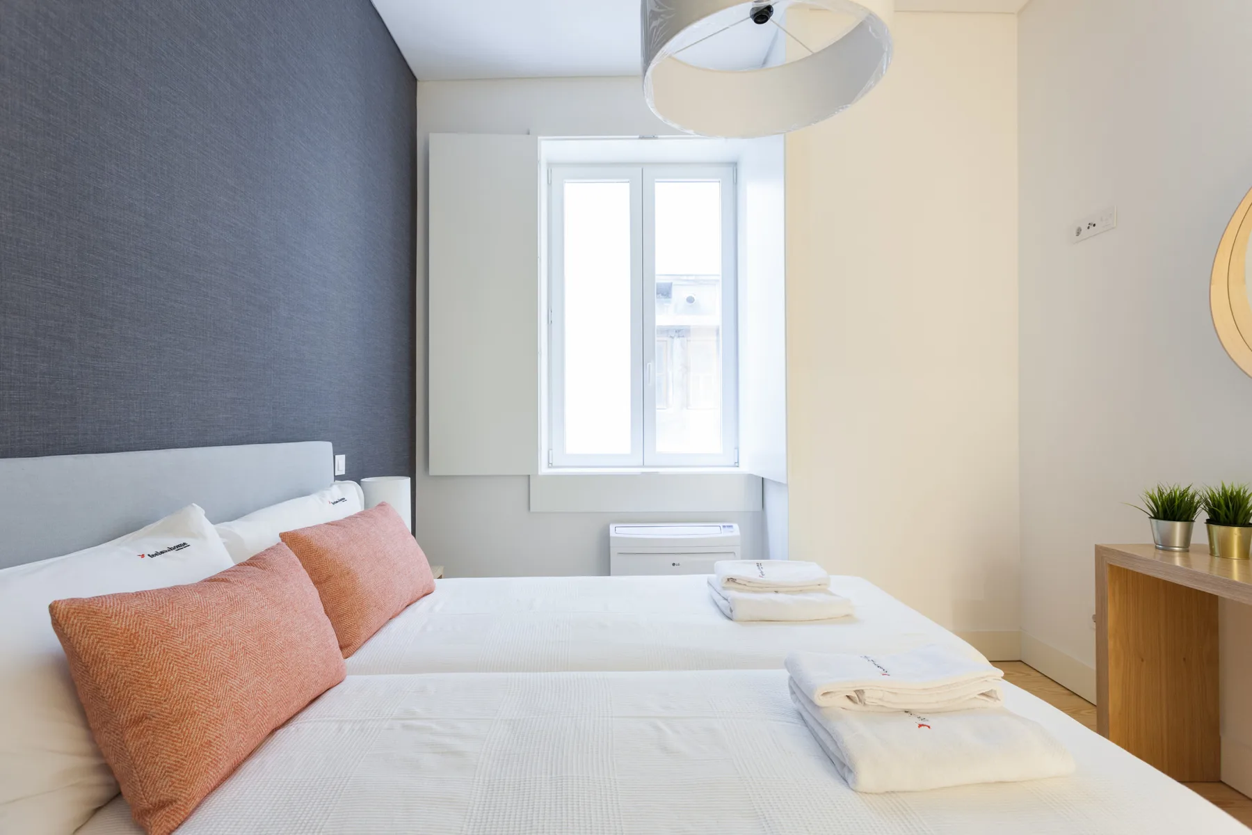 Un dormitorio con ropa de cama blanca, cojines color óxido y una ventana.