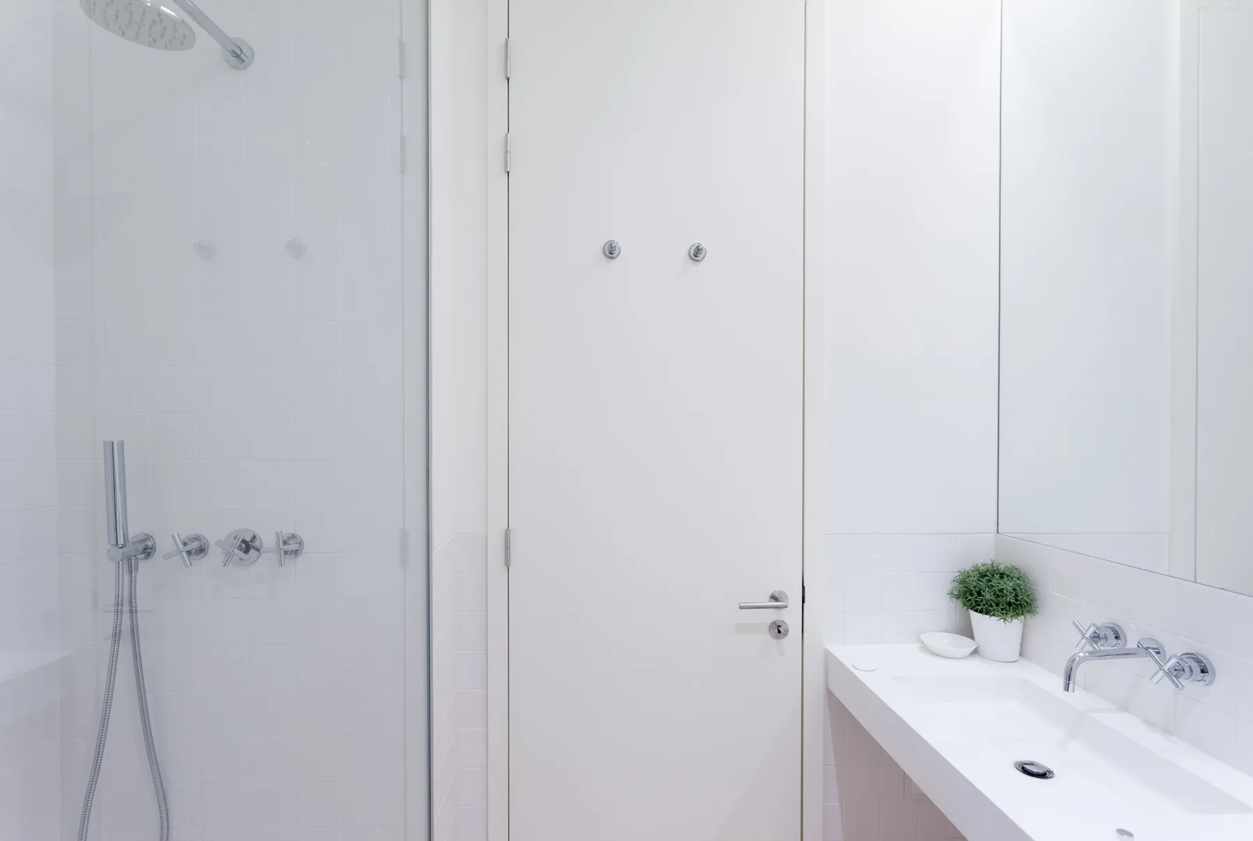 Un baño luminoso con ducha, lavabo y puerta blanca.