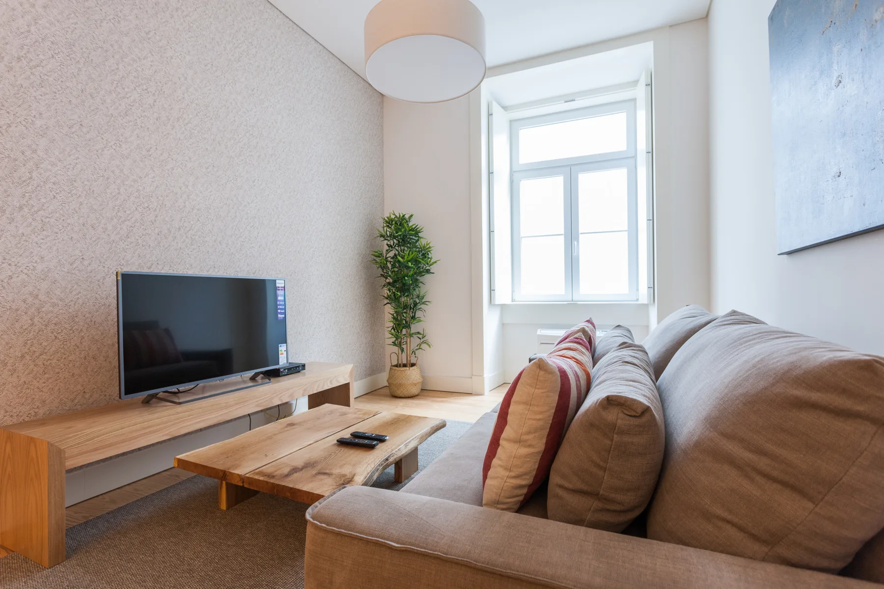 Una sala de estar con asientos, un televisor y una ventana luminosa.