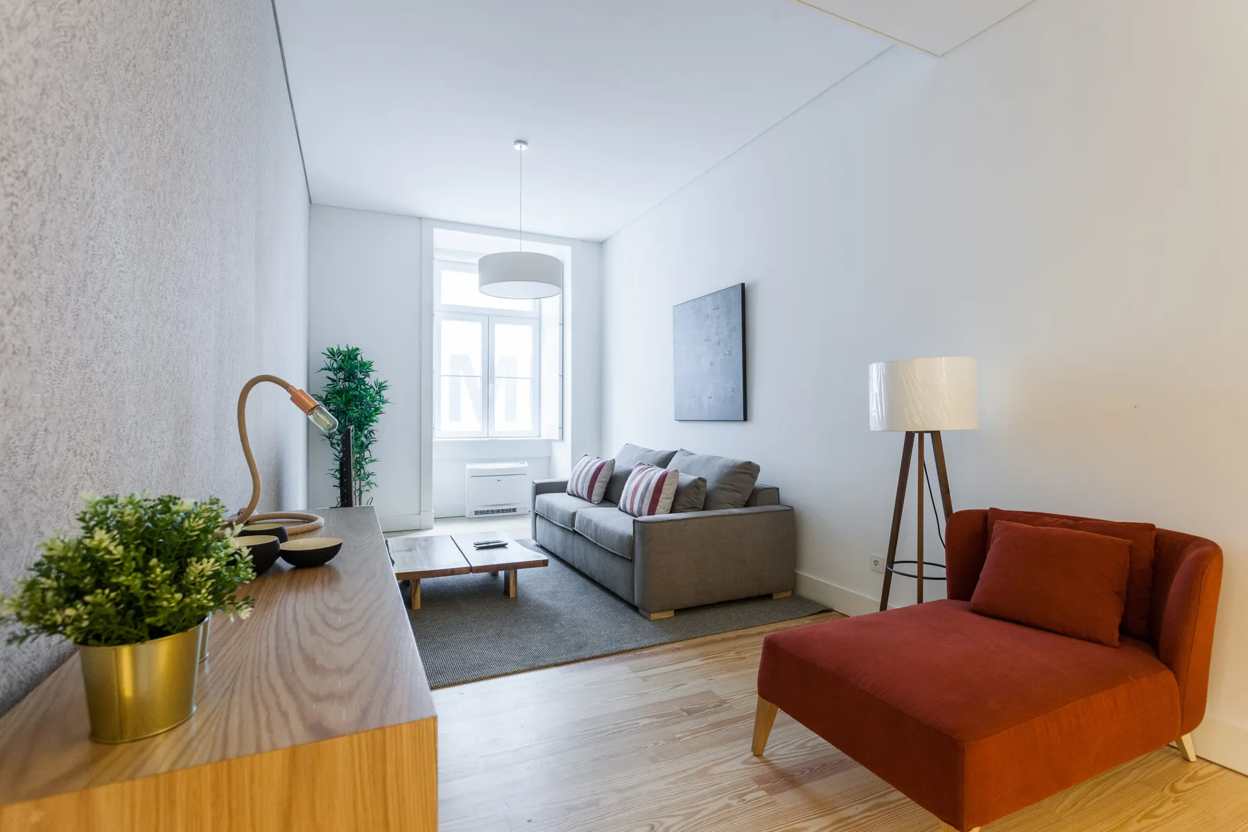A bright living room with a gray sofa, coffee table, and orange lounge chair.