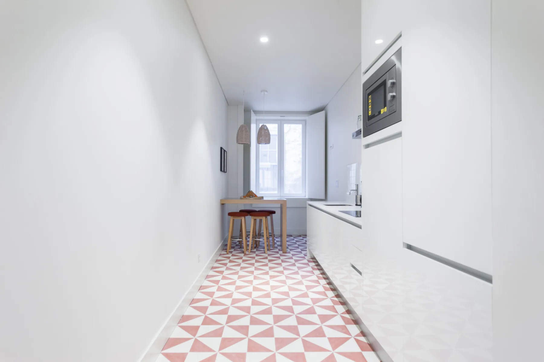 Una cocina estrecha con una pequeña mesa de comedor junto a una ventana luminosa.