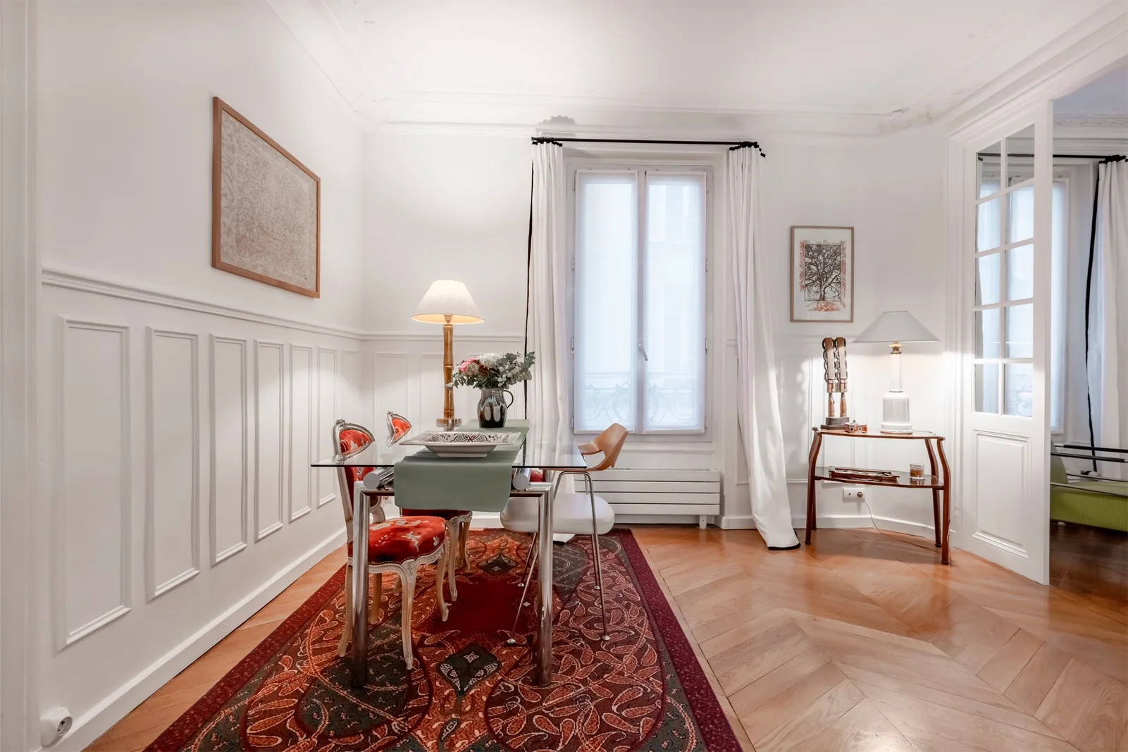 A bright sitting room with a dining table, patterned rug, and tall windows.