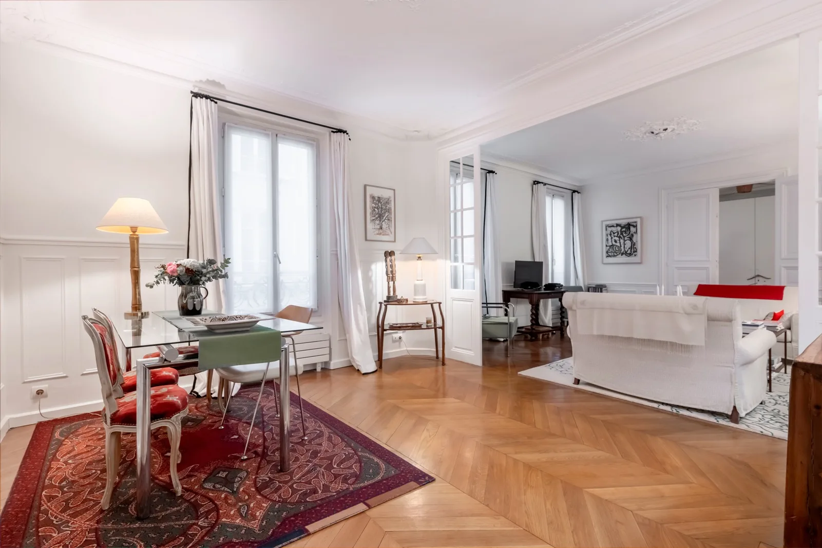 A bright living room with a dining table and seating beside tall windows.