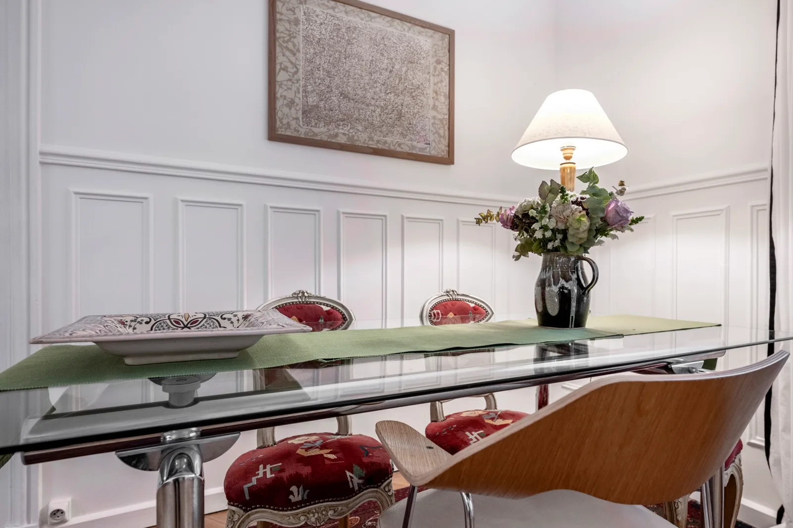 A dining area with a glass table, decorative seating, and a flower arrangement.