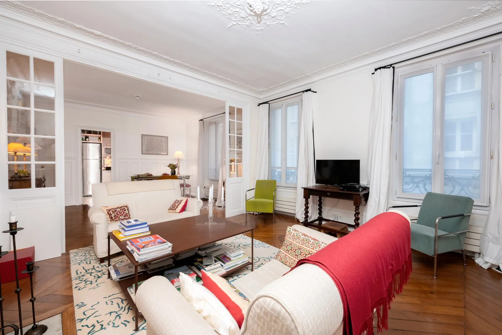 A bright living room with seating, a coffee table, and tall windows.