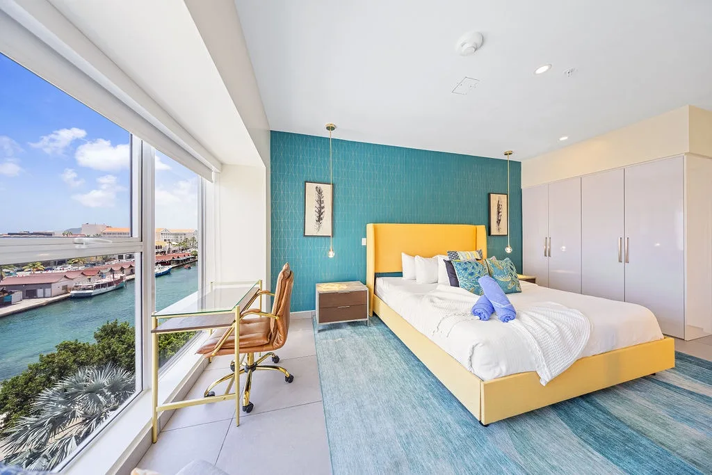 Wake up to stunning waterfront views from your vibrant, modern bedroom retreat, where plush linens, ocean-inspired hues, and a private workspace create the perfect coastal escape.