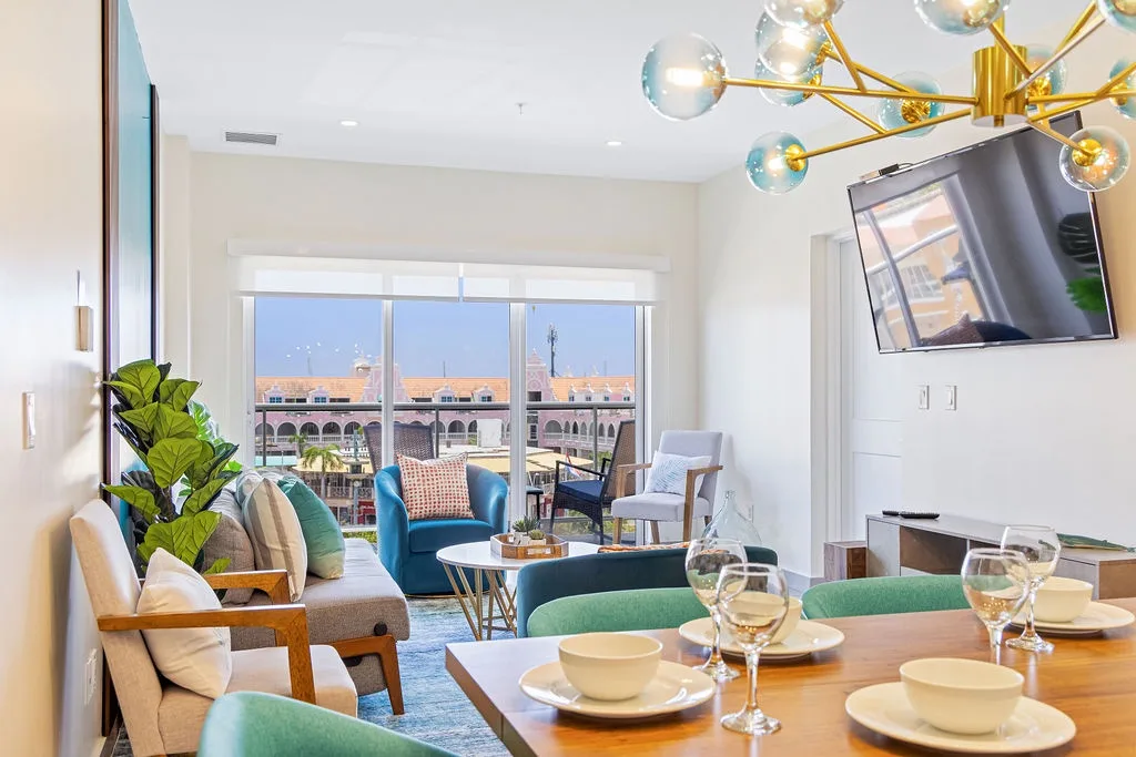 Picture yourself unwinding in this bright, modern living space where a chic dining table awaits your meals and a cozy sofa beckons you to relax as sunlight streams through windows framing charming views beyond.