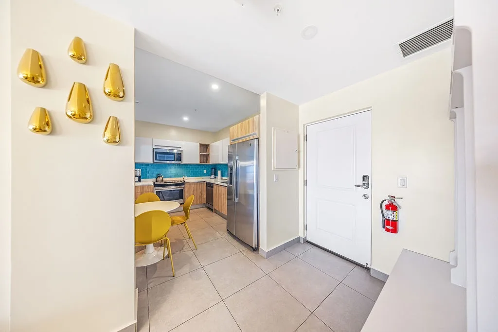 You'll love this cheerful, modern kitchen with vibrant blue backsplash, stainless appliances, and sleek golden accents that brighten your cooking space. The warm wood cabinetry and sunny yellow dining nook create a welcoming atmosphere for meals.