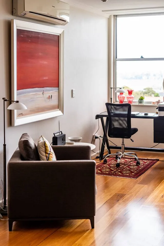 A living area with a desk and chair sits beside a large window.