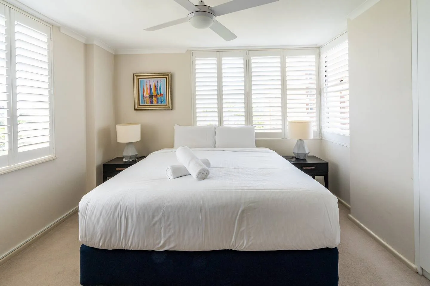 Un dormitorio luminoso con una cama grande y ventanas con contraventanas blancas.