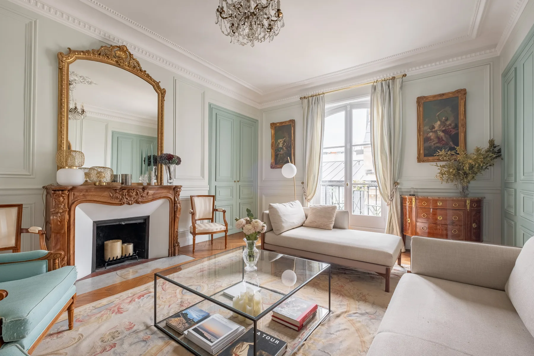 An elegant living room with a fireplace, seating, and tall windows.