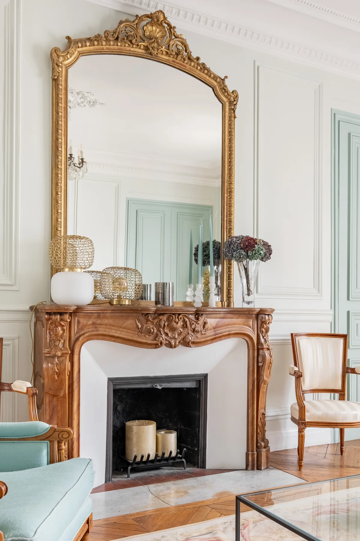 A decorative fireplace and ornate mirror stand in a bright sitting room.