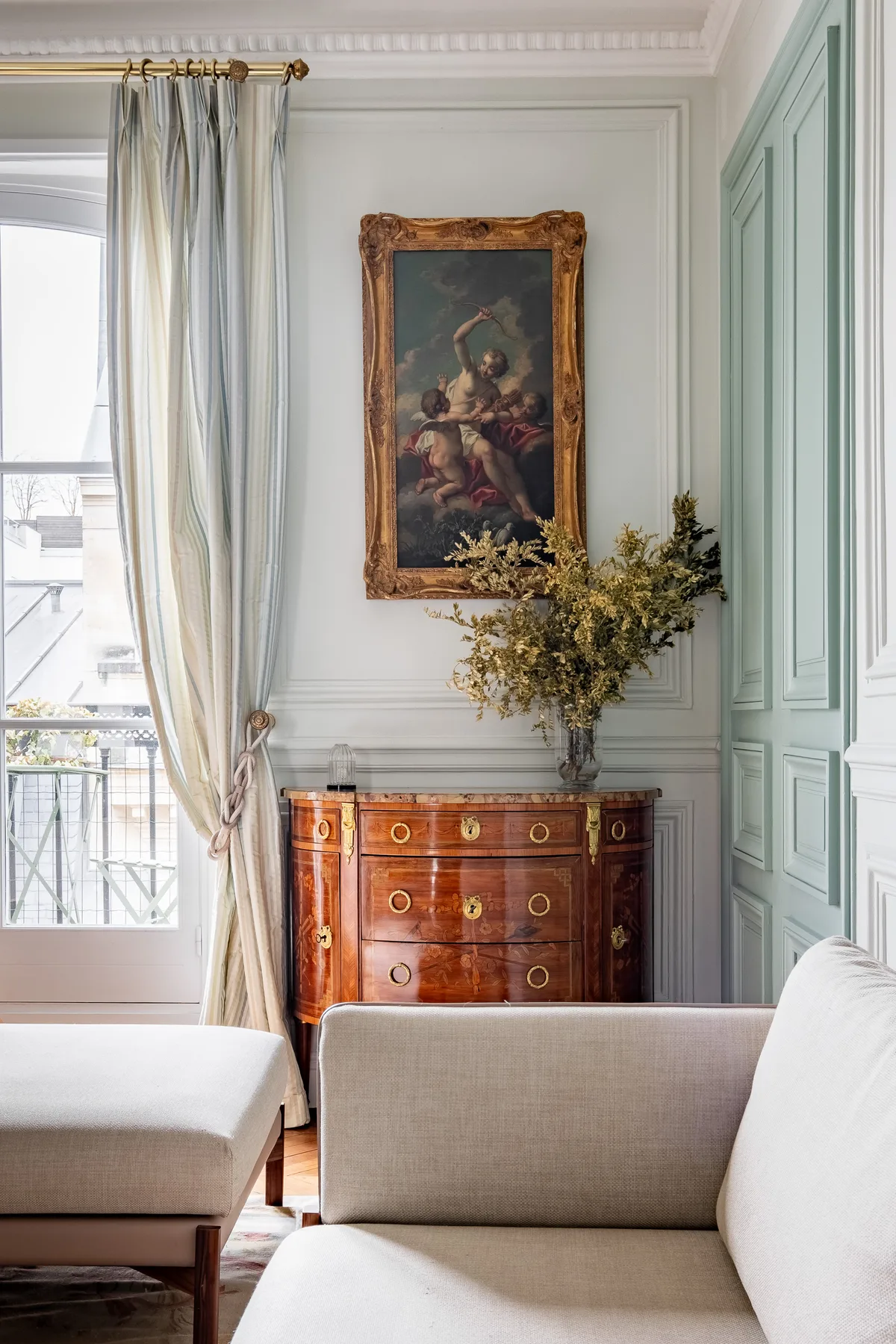 A bright sitting room with pale seating and a wooden chest beneath a framed painting.