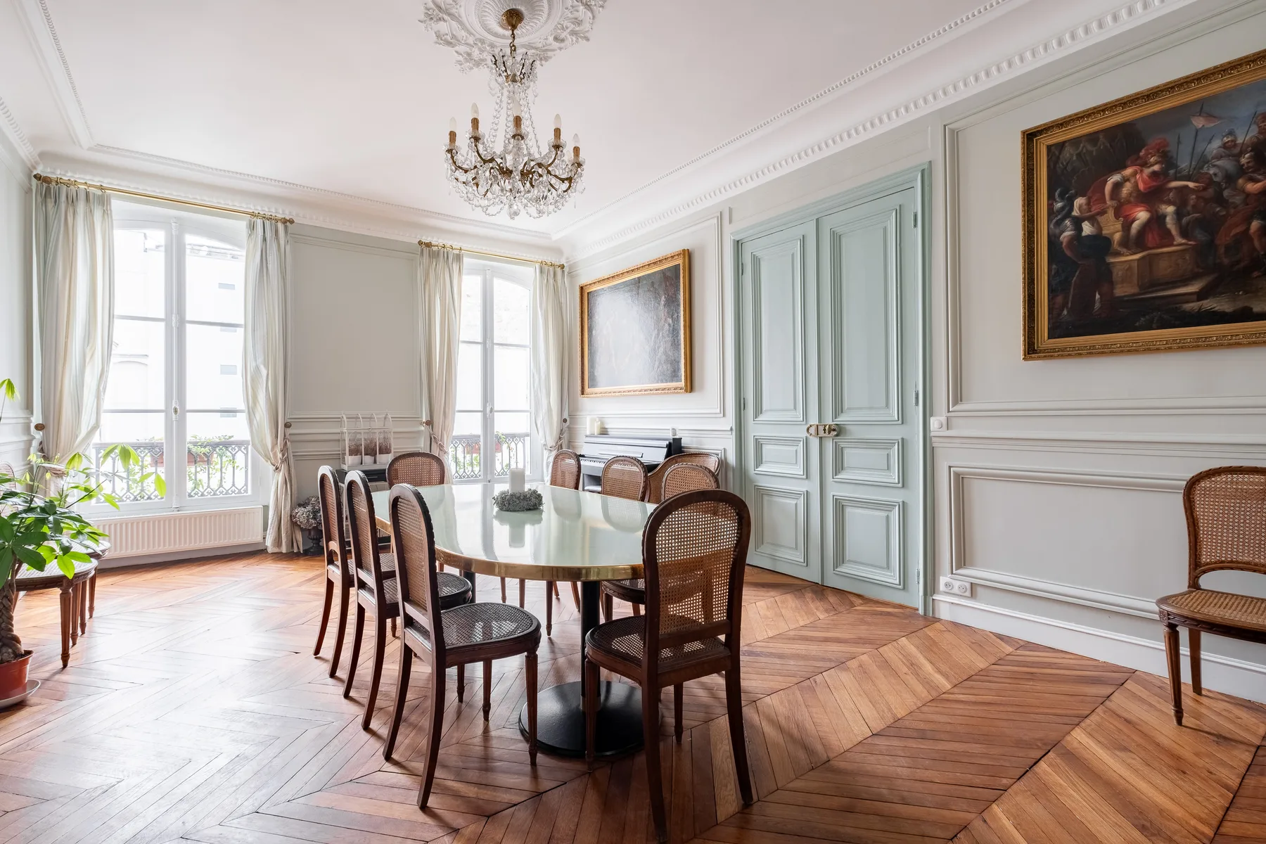 A formal dining room with a long table, chairs, and tall windows.