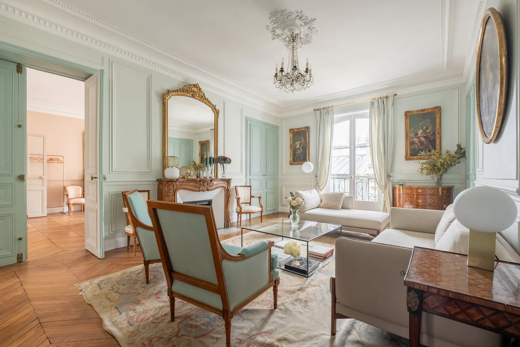A bright sitting room with pale green paneled walls and seating around a coffee table.