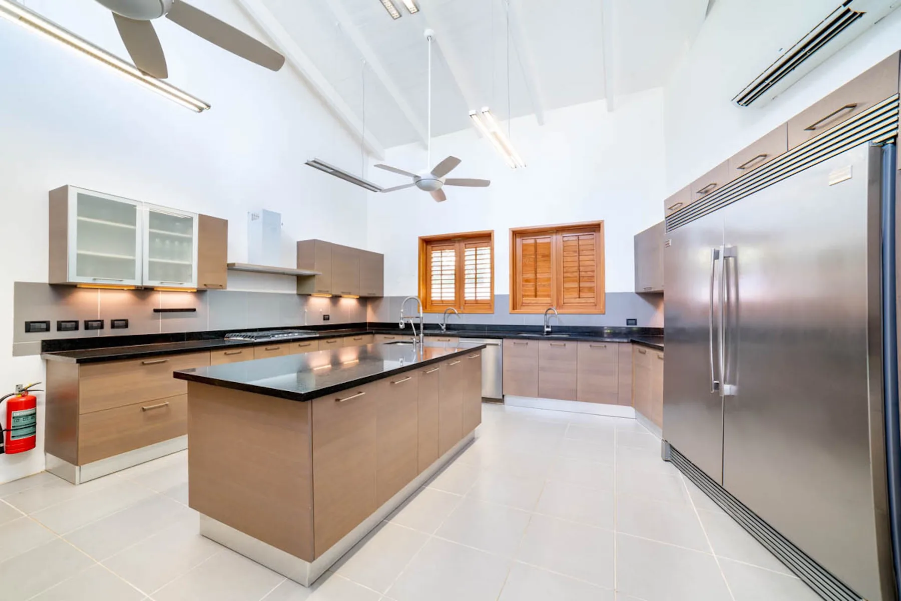 Una cocina amplia con isla central, refrigerador de acero inoxidable y persianas de madera.