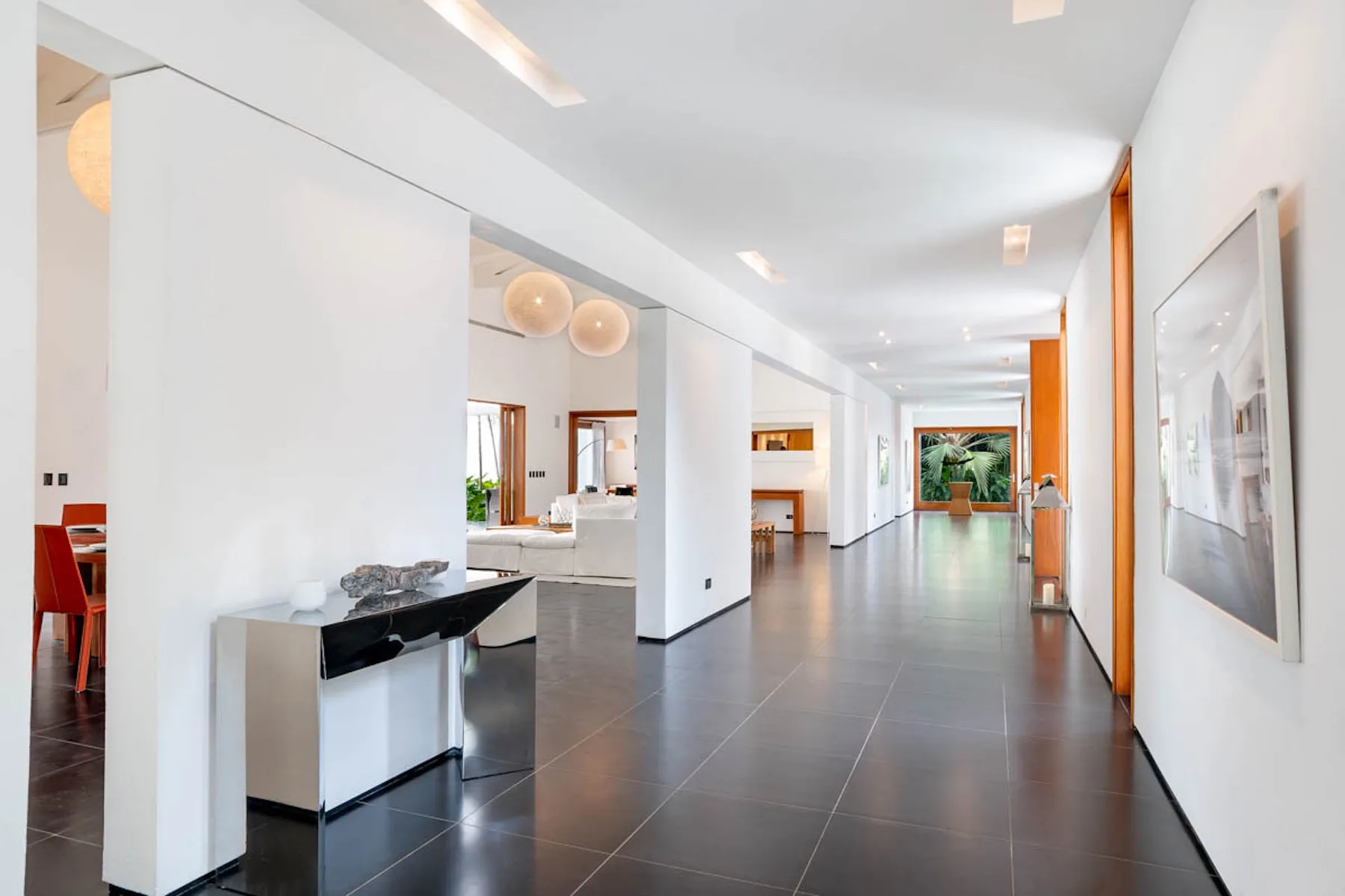 Un pasillo interior luminoso y moderno conduce a una zona de recepción con suelo de baldosas oscuras.