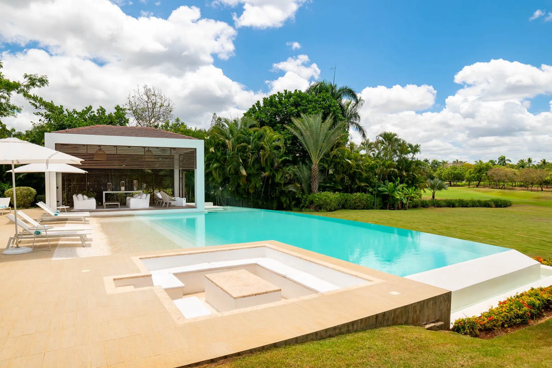 Una piscina al aire libre y una zona de estar hundida junto a un patio cubierto y vegetación.