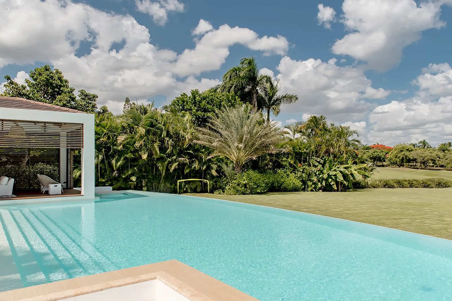 Una piscina al aire libre junto a un jardín frondoso bajo un cielo nublado.