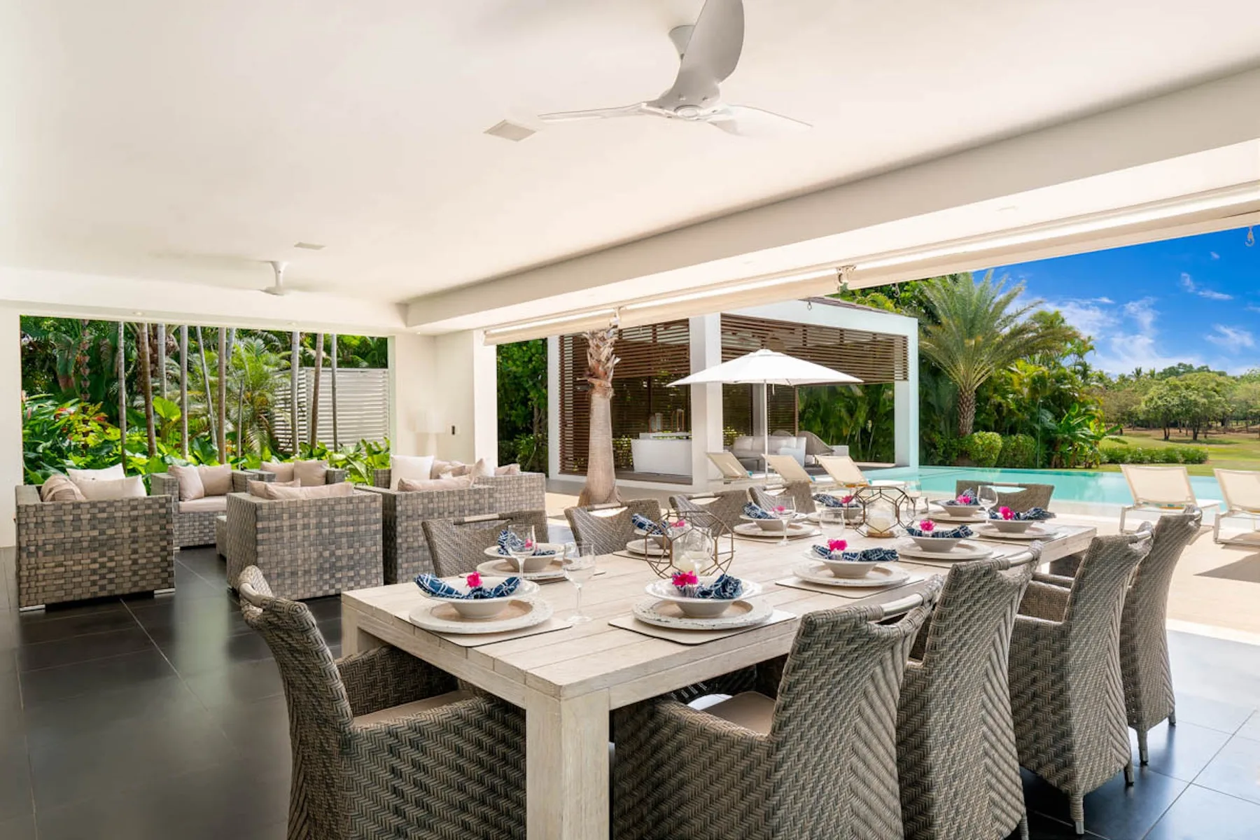Una zona de comedor exterior cubierta con una mesa larga frente a una piscina.