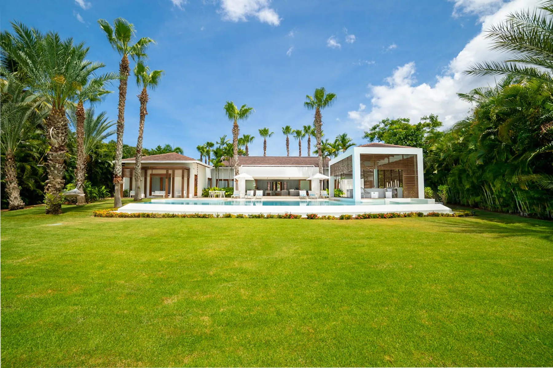 Una casa moderna da a un amplio césped verde, rodeada de palmeras.