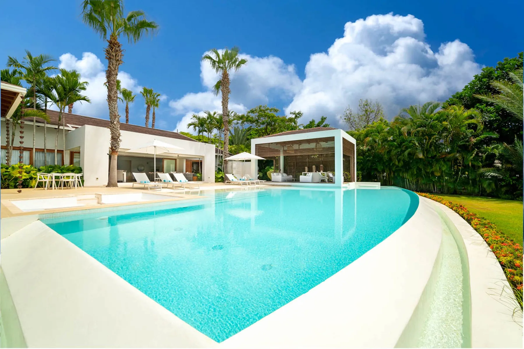 Una piscina curva junto a un edificio moderno y jardines.