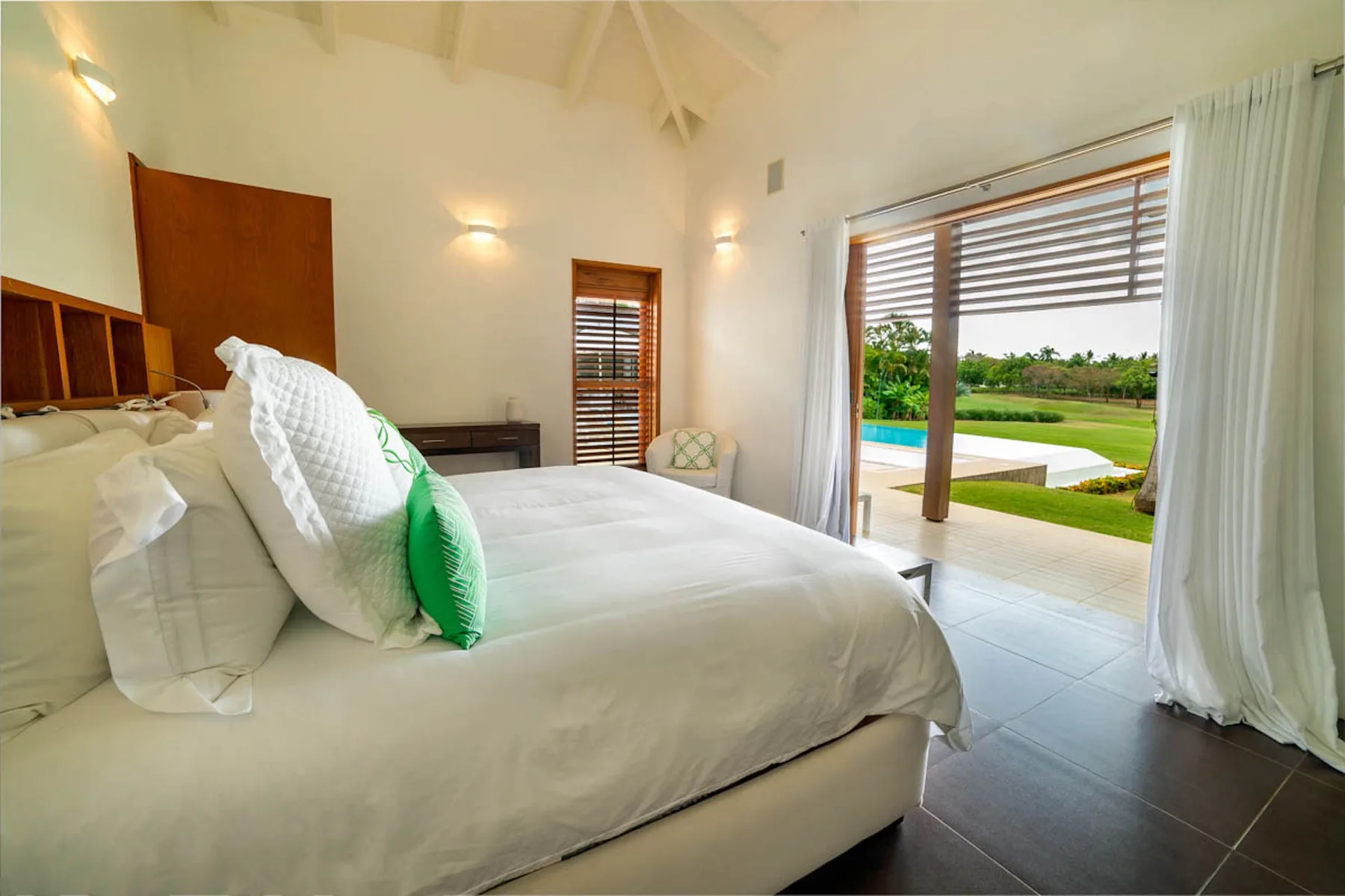 Un dormitorio con una cama grande y puertas corredizas abiertas hacia una piscina y un jardín.