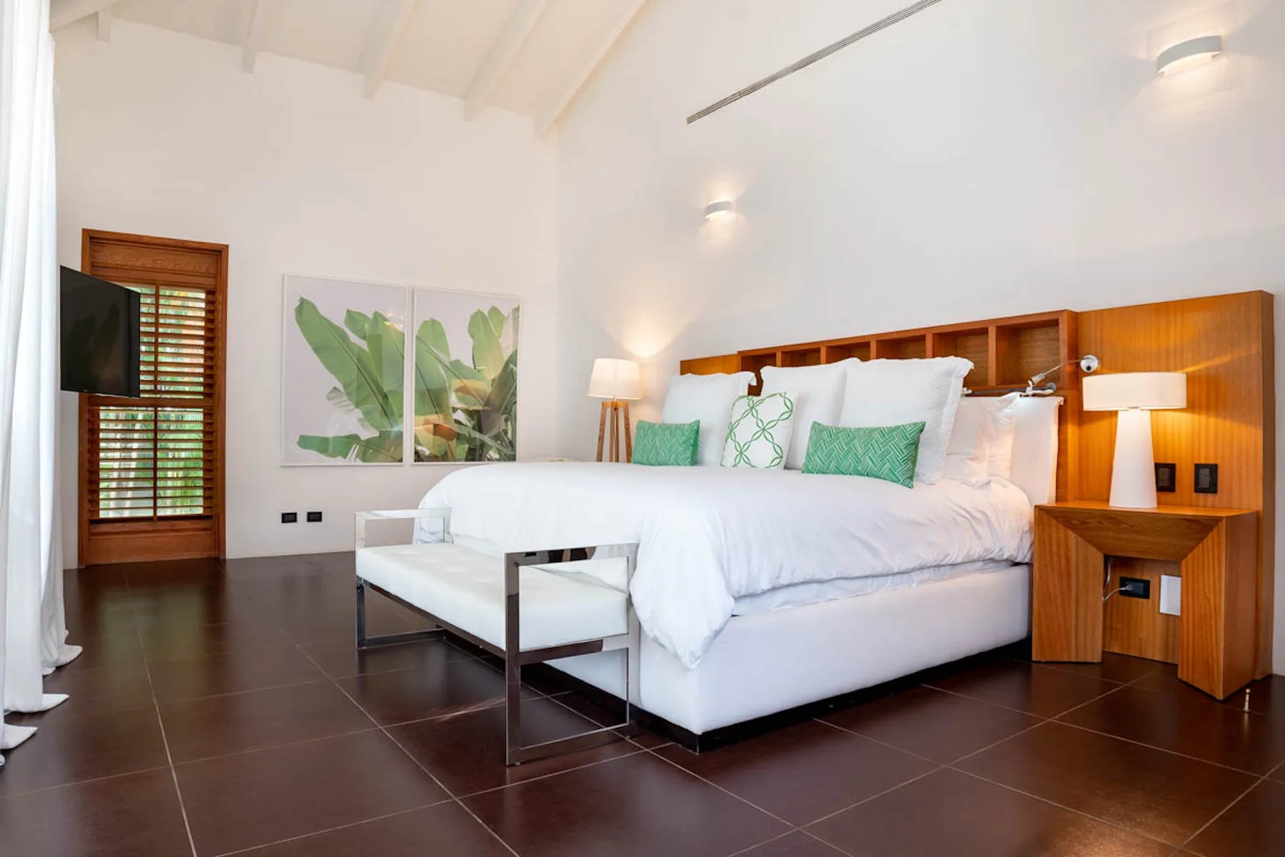 Un dormitorio luminoso con una cama blanca, cojines verdes y estanterías de madera junto a la cama.