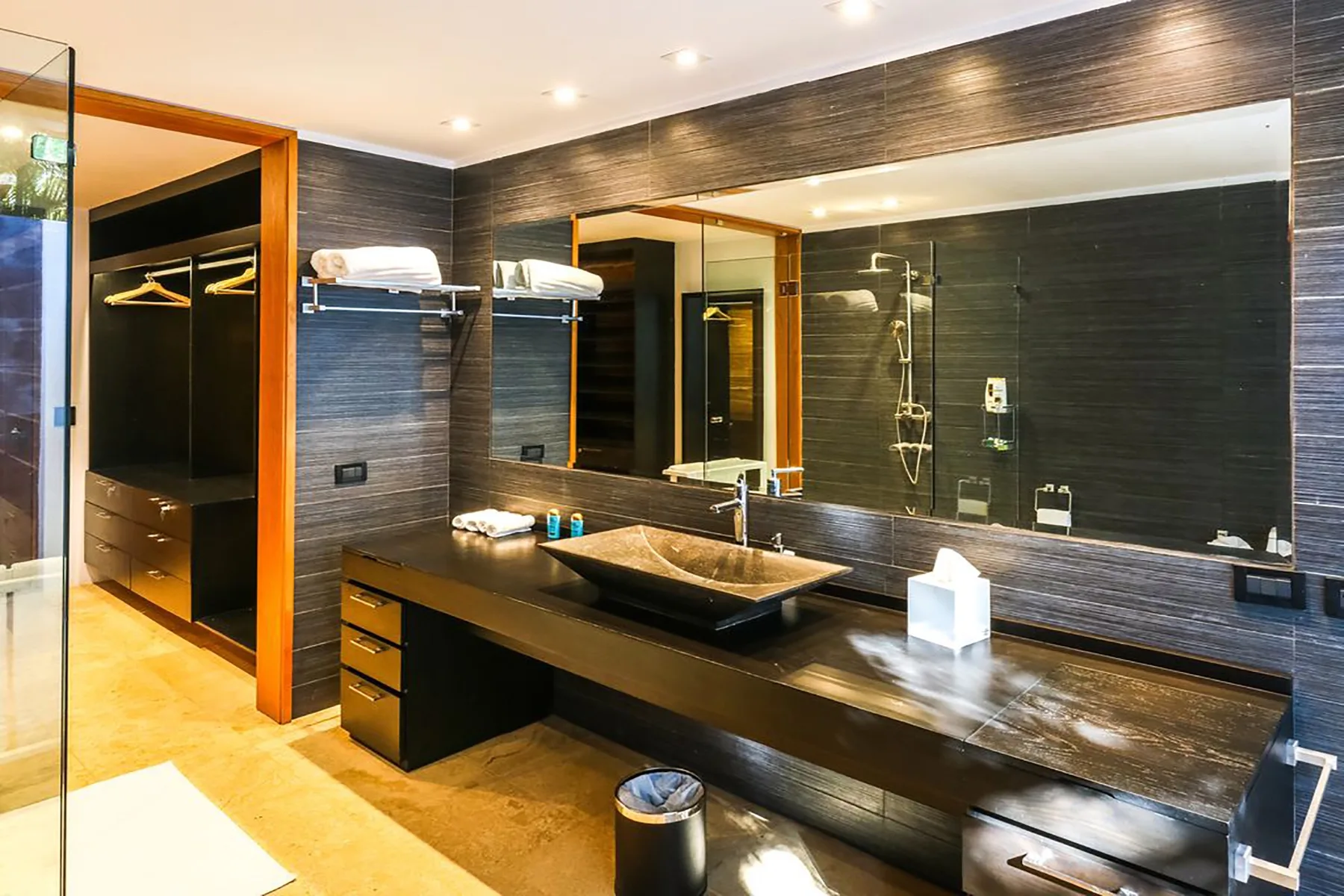 Un baño moderno con un tocador largo, un espejo grande y paredes de azulejos oscuros.
