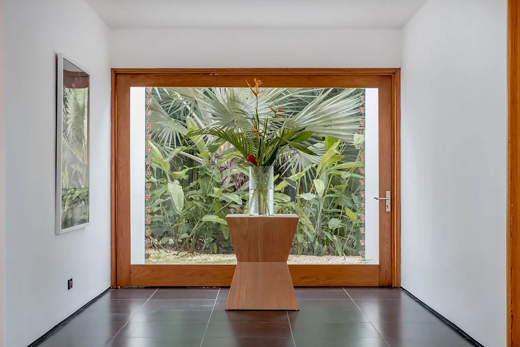 Un recibidor luminoso se abre a un jardín, con una planta sobre una mesa central.
