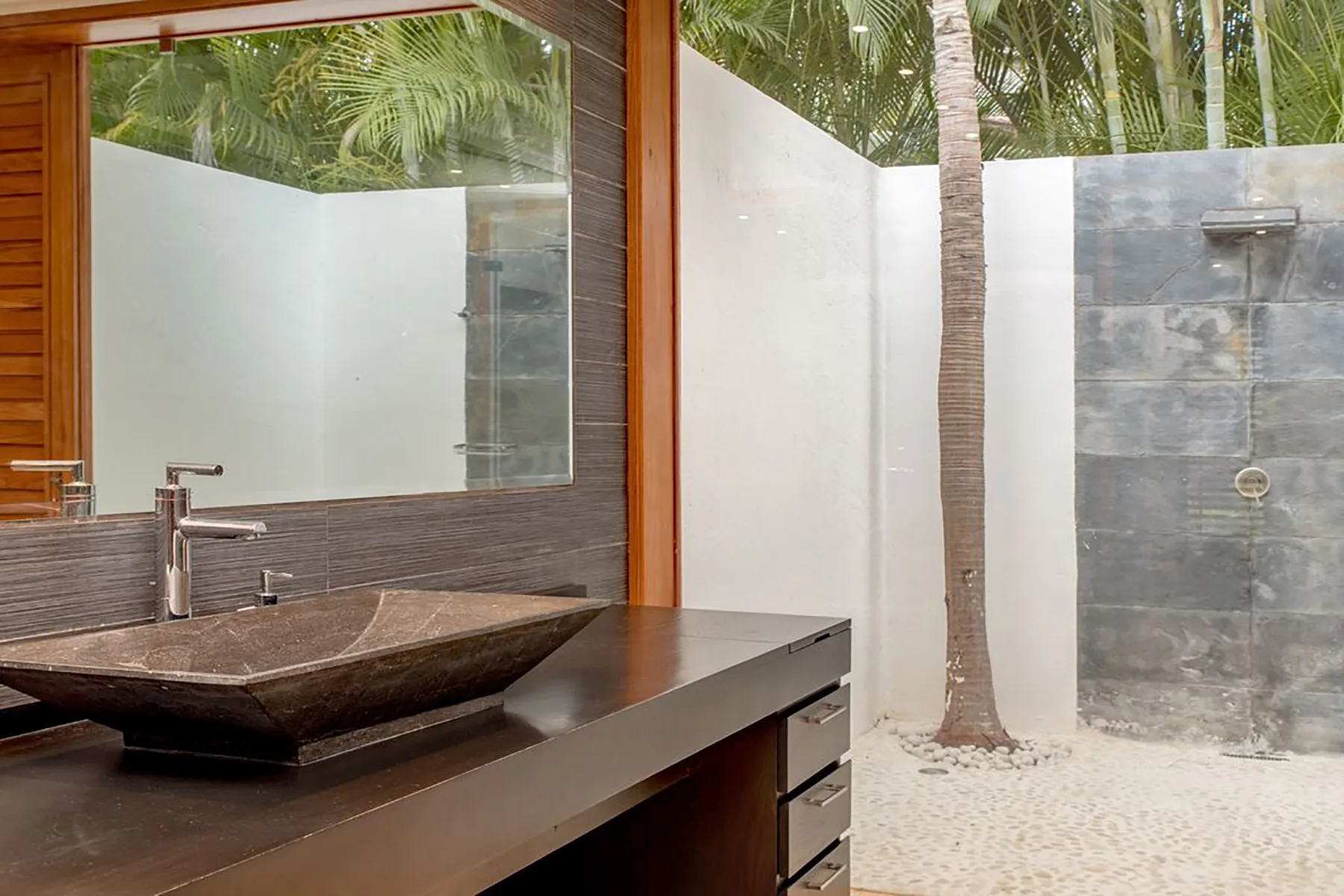 Un tocador de baño con lavabo sobre encimera da a una ducha al aire libre.