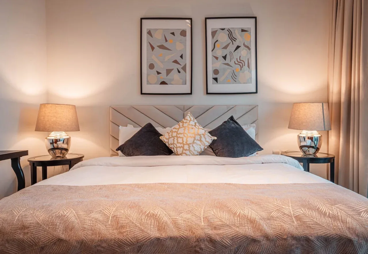 Un dormitorio con una cama tendida, cojines decorativos y cuadros enmarcados.