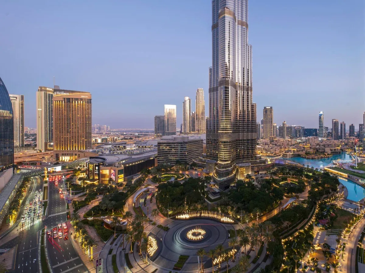 El horizonte urbano al atardecer rodea una torre alta y una plaza ajardinada.